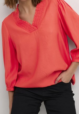 Koraalkleurige blouse met een V-hals en gerimpelde details bij de halslijn. Driekwartmouwen met gathered manchetten. Zachte, gladde textuur.