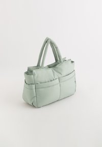 Gepolsterte Handtasche aus weichem grünen Stoff, mit zwei kurzen Tragegriffen, rechteckiger Form und sichtbaren Nähakzenten auf der Oberfläche.