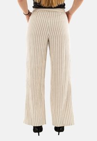 Pantaloni a gamba larga color crema con righe verticali nere, caratterizzati da un alto punto vita e da una texture di tessuto liscia. Scarpe con tacco alto nere visibili.