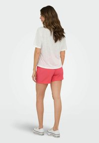 Witte T-shirt met korte mouwen gecombineerd met een roze broekje. Model draagt witte sneakers. Zichtbare stofstructuur en casual silhouet.