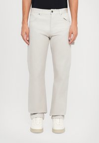 Lichtgrijze rechtlopende broek van katoen, met voorzakken, een knoopsluiting en een subtiele textuur. Gekoeld met witte sneakers.