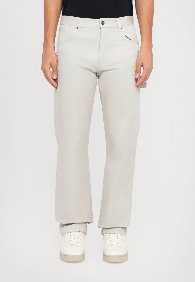 Pantalons droits gris clair en coton, avec poches avant, fermeture à bouton et texture subtile. Associés à des baskets blanches.