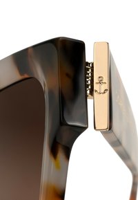 Sluneční brýle v želvovinovém designu s robustním rámem, hnědými skly a zlatými detaily, na bočním pantu s kotvou.