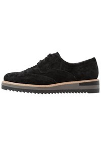 Černá semišová obuv s designem wingtip, obsahující perforované detaily, béžovou mezipodešev a texturovanou černou gumovou podrážku.