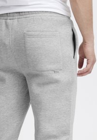 Gray cotton sweatpants featuring side pockets and a back pocket, with a small branded label displayed near the waistband.