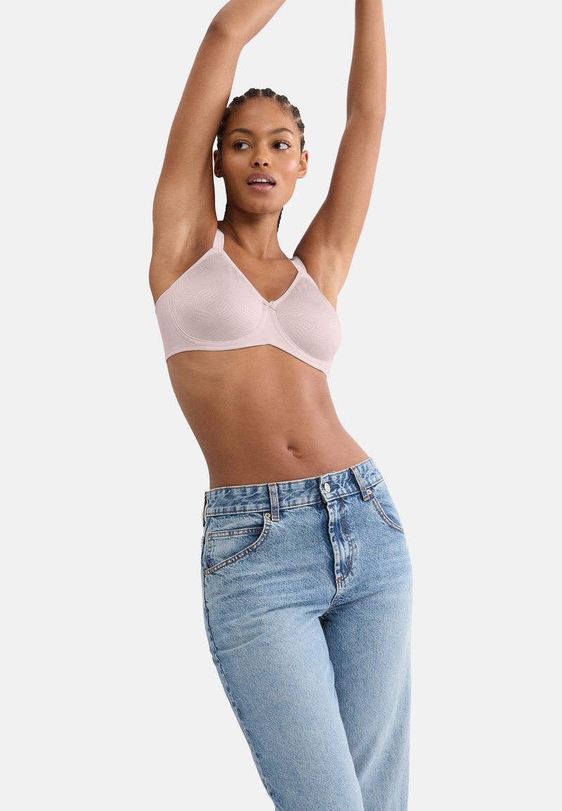 Ανοιχτό ροζ σουτιέν με υφή υφάσματος,  ρυθμιζόμενους ιμάντες και κλείσιμο με αγκράφα. Συνδυάζεται με ψηλόμεσα μπλε τζιν παντελόνια.