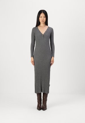 Robe en tricot côtelé gris avec des manches longues, un décolleté en V, des accents de boutons et des fentes latérales, assortie à des bottines brunes.