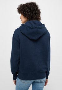 Felpa con cappuccio di colore blu navy realizzata in morbido cotone, dotata di cappuccio con cordini, maniche lunghe e polsini a costine, con una vestibilità comoda e una texture liscia.