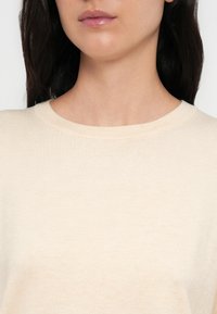 Μπεζ, ελαφρύ πουλόβερ με στρογγυλή λαιμόκοψη, ριμπ ύφασμα και διακριτικές ραφές. Λείο ύφασμα, εφαρμοστό σχέδιο, κοντά μανίκια.