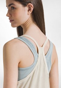 Dva nátělníky na sobě: světle modrý žebrovaný top s tenkými ramínky, krémový volný nátělník se širšími ramínky, hladká látka, neformální design.