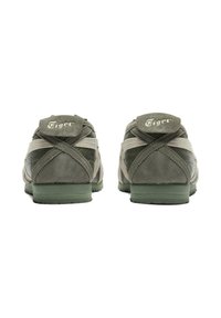 Green suede sneakers with white accents, featuring a textured finish, cross-stitched details, and a raised logo label on the heel.