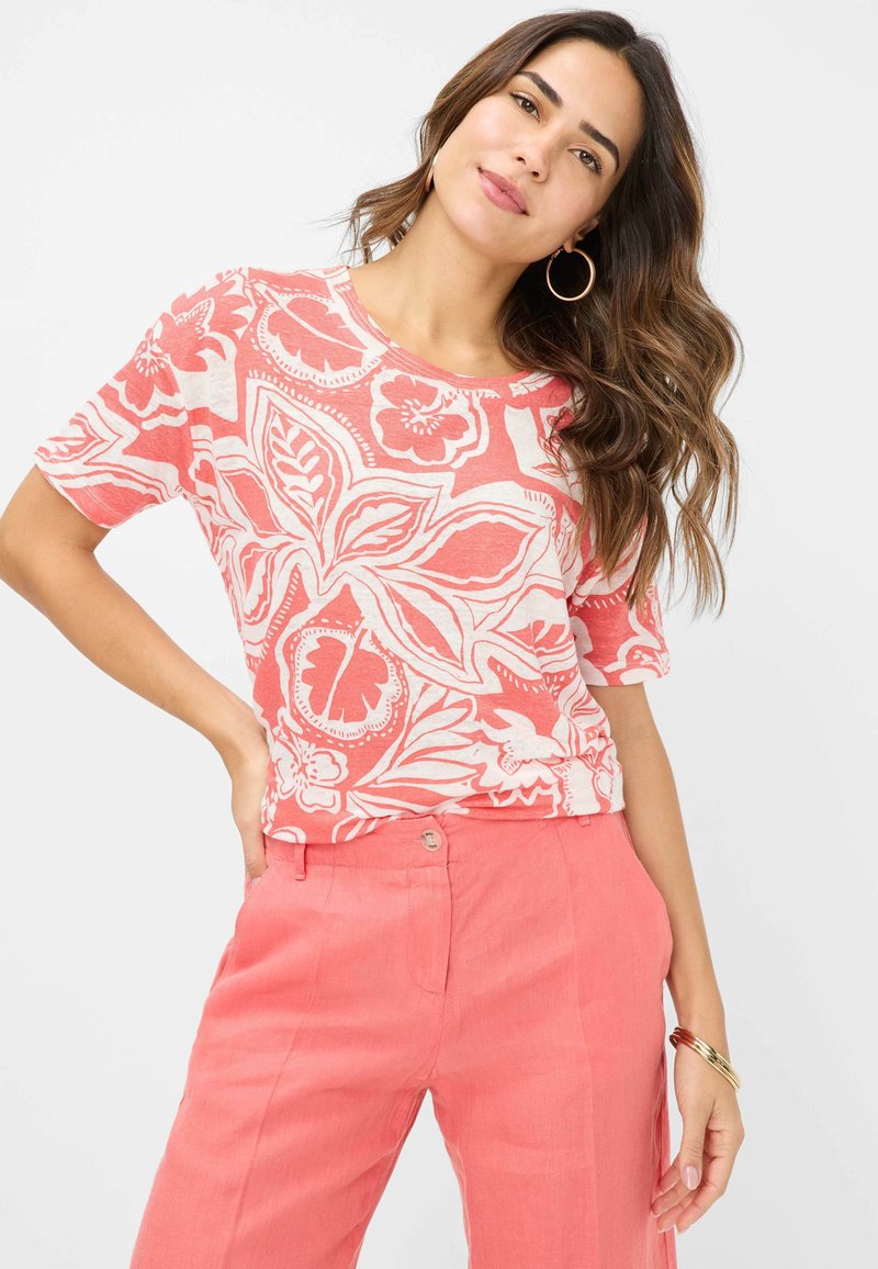 Korallefarbener Kurzarm-Top mit einem auffälligen floralen und blätterartigen weißen Muster; kombiniert mit passenden korallefarbenen Hosen, die eine lockere Passform zeigen.