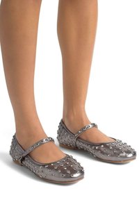Bailarinas metálicas plateadas con acentos de tachuelas redondas, que presentan una correa estilo Mary Jane. Textura suave con una suela flexible y punta redondeada.