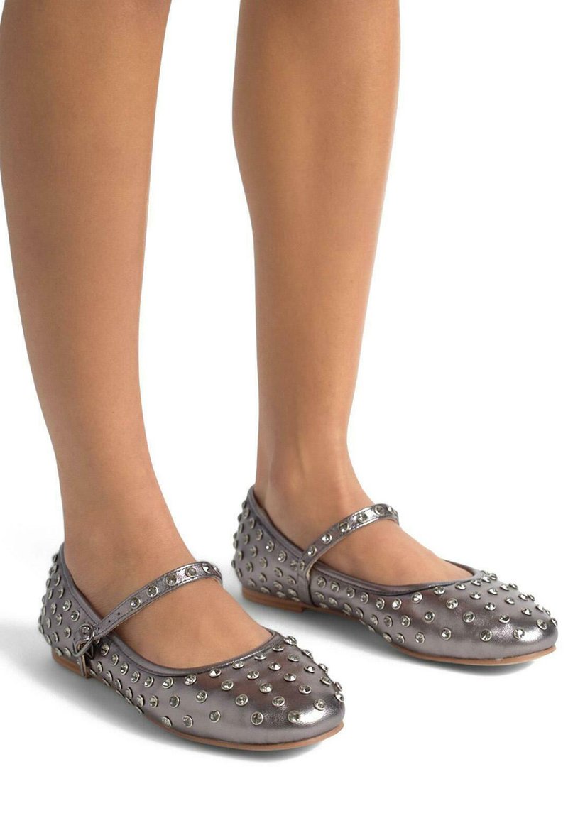 Bailarinas metálicas plateadas con acentos de tachuelas redondas, que presentan una correa estilo Mary Jane. Textura suave con una suela flexible y punta redondeada.