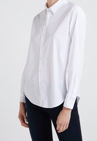 Camicia bianca con bottoni realizzata in cotone morbido, caratterizzata da un colletto classico, maniche lunghe con polsini a bottone e un orlo curvo.