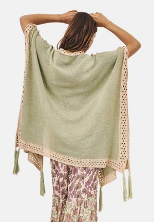 Poncho verde claro de corte holgado, decorado con un ribete de encaje crema y borlas en las esquinas, con una textura de punto suave.