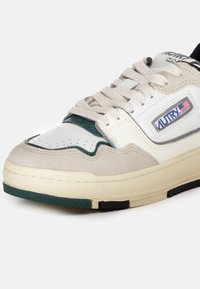 Sneaker con una toma in pelle bianca, accenti verdi e sovrapposizioni in suede beige. Caratterizzata da una suola in gomma testurizzata e un sistema di allacciatura. Marchio Autry visibile.