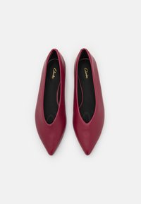 Ballerines en cuir bordeaux avec un nez pointu et un design à enfiler. Dotées d'un intérieur noir et d'une texture lisse. Nom de la marque visible à l'intérieur.