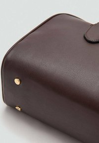 Hnedá kožená taška má textúrovaný povrch, zaoblený tvar a zlaté ozdoby. Na spodnej strane sú malé zlaté cvoky.