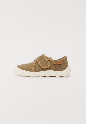 Sapatilha de tecido castanho com fecho de velcro, sola branca, superfície texturizada e uma pequena etiqueta de couro na lateral.