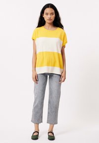 Korte mouwen gele en witte gestreepte top, lichtgrijze broek met rechte pijpen, groene flats met zwarte bandjes. Eenvoudige, ontspannen pasvorm.