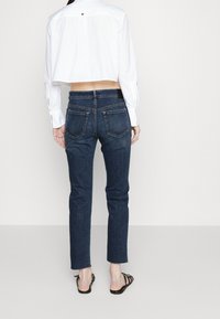 Tmavě modré džínové kalhoty slim fit, s středním pasem a dvěma zadními kapsami. Kombinované s zkrácenou bílou košilí a sandály.