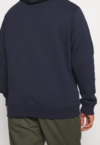 Felpa navy blu con una texture morbida, cappuccio regolabile, polsini e orlo a coste, caratterizzata da un design posteriore semplice e senza cuciture.