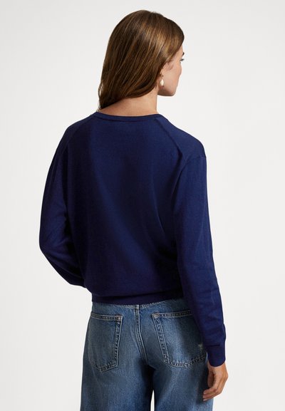 Camisola de malha azul-marinho com mangas compridas e decote arredondado, combinada com jeans de ganga azul claro. O tecido parece suave e macio.