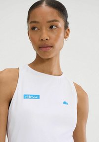Biała bluzka bez rękawów z niebieskim logo "ellesse" oraz małym niebieskim akcentem. Gładki materiał o dopasowanym kroju, bez widocznych wzorów.