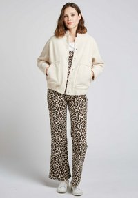 Veste en polaire crème avec des boutons pression et deux poches avant, associée à un pantalon évasé imprimé léopard marron et noir et des baskets blanches.
