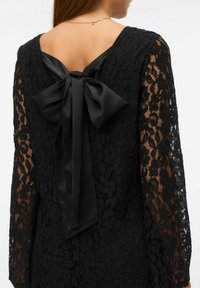 Mustast pitsist kleit pikkade varrukatega ja sügava tagakaelusega. Seljal on suur satiinist lakk, mis lisab kleidile detaili.