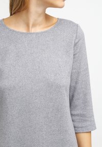 Grå tröja med en texturerad, mjuk tyg. Har en bred rund halsringning och trekvartsärmar. Sömlös design med minimal detaljering.