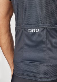 Tricou de ciclism gri închis cu textură din plasă și talie elastică. Dispune de un buzunar posterior și un logo alb "GIRO" pe spate.