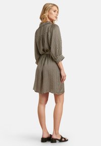 Schwarz-beige gestreiftes Kleid im Chevron-Muster mit Dreiviertelärmeln, tailliertem Schnitt und schwingendem Rock. Schwarze Sandalen mit Blockabsatz.