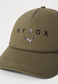 Klobouk olivové barvy se strukturovaným designem, na přední straně s nápisem "HYROX" v černé barvě a reflexním stříbrným logem Puma. Texturovaná tkanina.