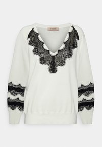 Weißer Pullover mit tiefem V-Ausschnitt und schwarzem Spitzenbesatz am Halsausschnitt und an den Ärmeln. Er hat einen gerippten Saum und eine weiche Textur.