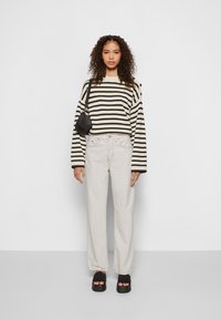 Suéter de malha riscas preto e branco, jeans bege claro, mala de ombro preta e sandálias de plataforma pretas. Conjunto casual com jeans de perna larga.