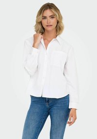White button-up shirt with long sleeves, a collar, and a front pocket. Made from a lightweight fabric with a slightly textured finish.