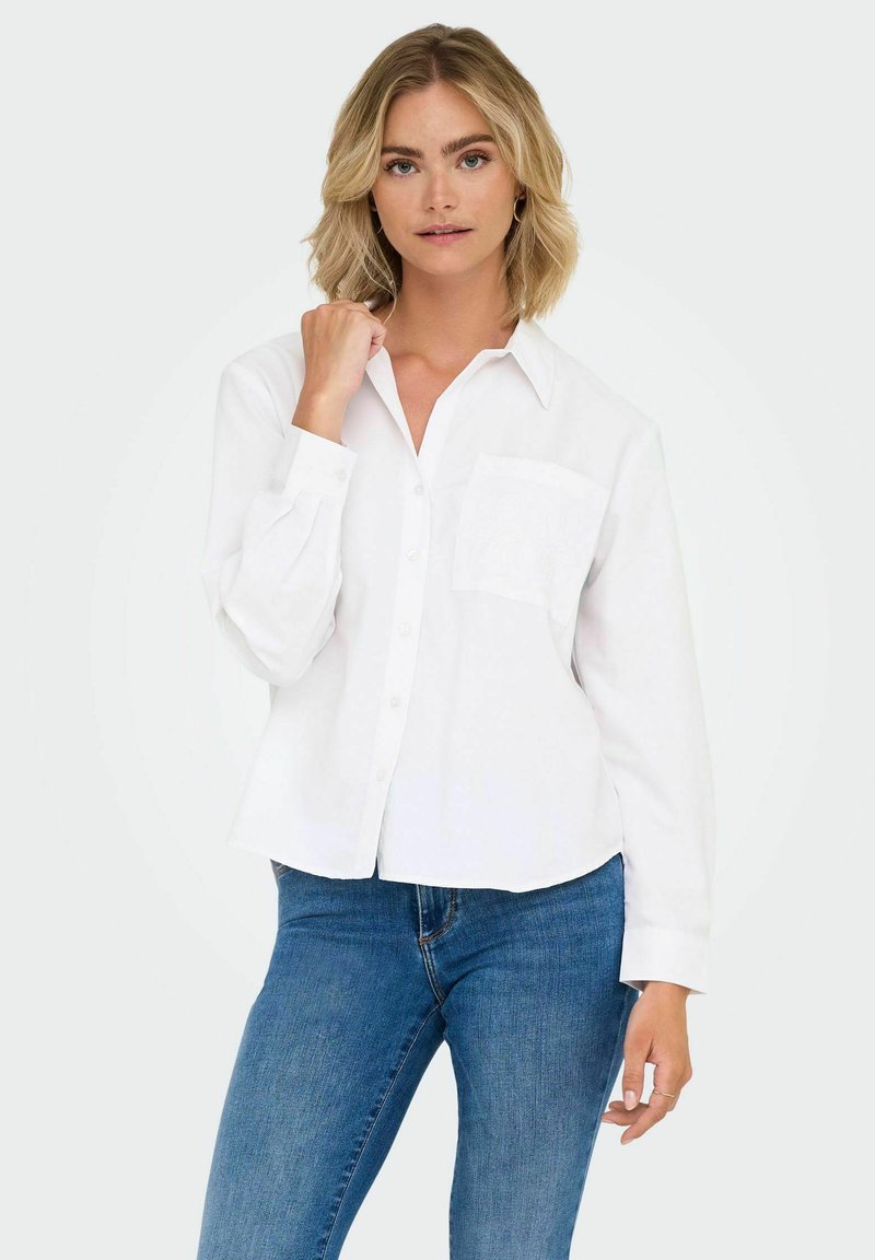 White button-up shirt with long sleeves, a collar, and a front pocket. Made from a lightweight fabric with a slightly textured finish.