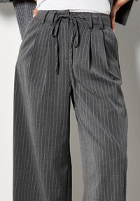 Pantaloni grigi a righe sottili con taglio morbido, vita elastica e chiusura con lacci. Texture morbida con pieghe visibili e tasche.