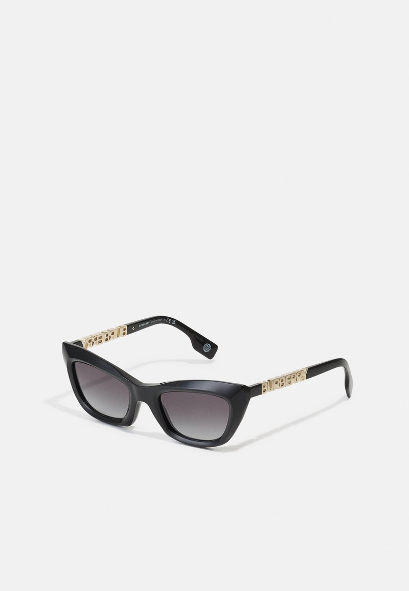Melna kaķa acs saulesbrilles ar gradienta lēcām un zelta toņa zīmola akcentiem uz tempļiem. Elegants plastmasas rāmis ar asiem stūriem.