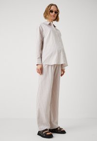 Chemise à rayures claires avec col, associée à un pantalon large. Tissu texturé, couleurs beige doux et crème, portée avec des sandales noires.