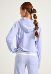 Jasnofioletowa bluza z kapturem o miękkiej fakturze, z długimi rękawami, zestawiona z pasującymi dresami z tylnymi kieszeniami.