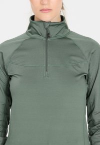 Lättvikts, mörkgrön kvartsglipa med en upphöjd krage, strukturerad tyg och plattlock sömmar för komfort och flexibilitet.