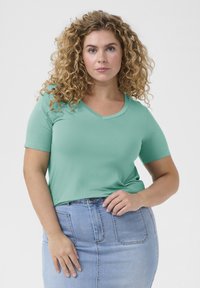 T-shirt z krótkim rękawem w miętowym kolorze z dekoltem w serek, wykonany z miękkiego materiału, w połączeniu z jasnoniebieską spódnicą dżinsową z przednimi kieszeniami i dopasowanym krojem.