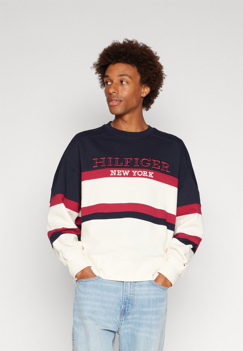 Felpa blu navy e crema con strisce rosse e logo "HILFIGER NEW YORK". Presenta un collo a giro e una vestibilità comoda, realizzata in tessuto morbido.
