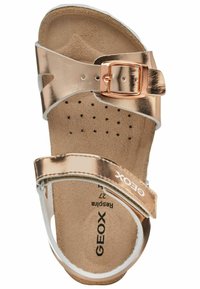 Roze gouden metallic sandaal met verstelbare band, gespsluiting en tan gekussen voetbed. Witte accenten en een geperforeerd zoolontwerp aanwezig.