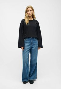 Sudadera negra con bordado floral, mangas anchas; combinada con jeans de mezclilla azul de tiro alto y corte holgado; textura suave y ajuste casual.