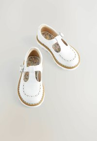 Chaussures en cuir blanc avec un design découpé, des perforations en forme d'étoile et une boucle ronde. Semelles intérieures à motif floral et semelles en caoutchouc beige.