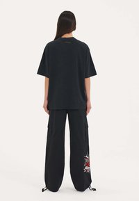 Zwarte oversized t-shirt met korte mouwen, gecombineerd met zwarte cargobroek met een rood geborduurd ontwerp en verstelbare enkelstrikken.